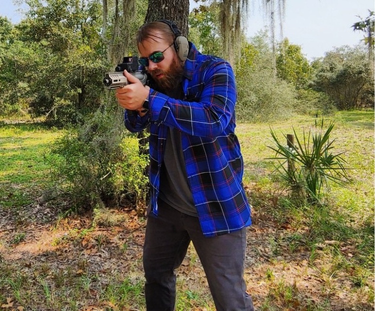 Travis Pike wearing a flannel shirt, aiming a CMMG Banshee.